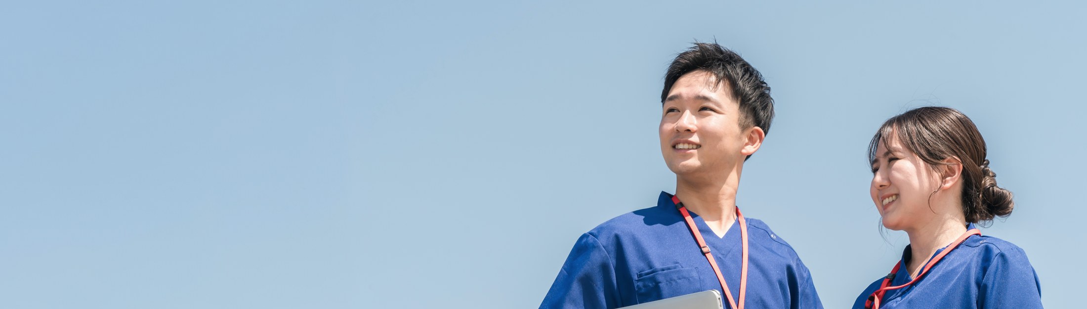 スクラブを着た看護師と保健師が、青空の下で前を見つめている様子